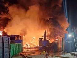 Firefighters battle massive night-time blaze at industrial site with burning warehouse, cranes, and vehicles